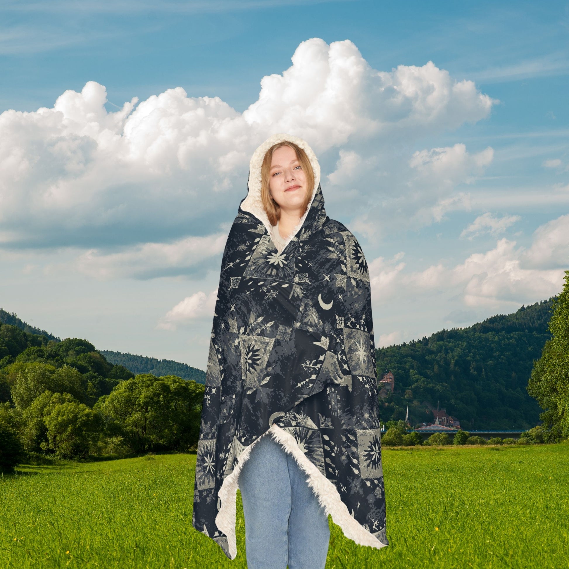 Person wrapped in a patterned blanket standing in a field with mountains in the background