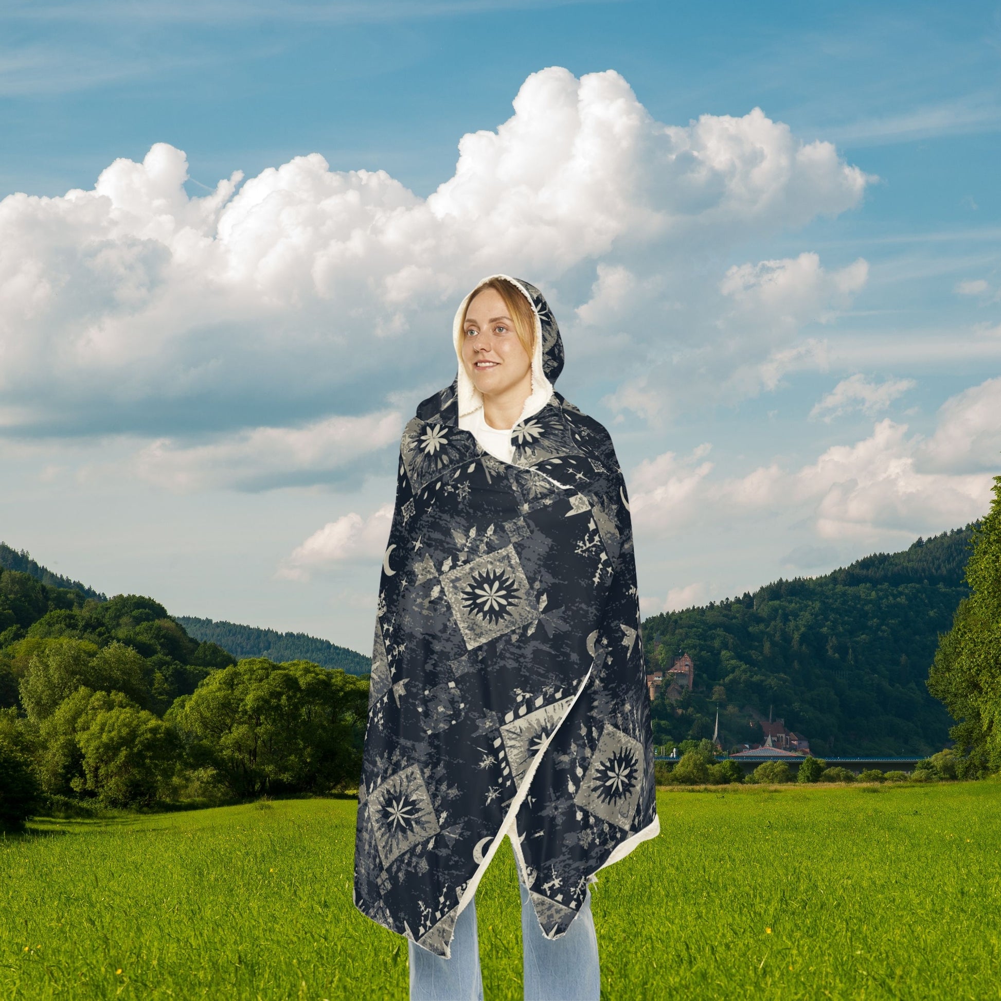 Person wearing a patterned poncho in a green field with mountains and blue sky.